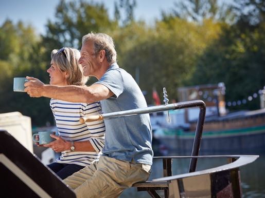 A man and a woman having a cup of tea on top of a canal boat