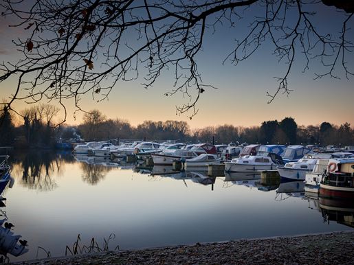 Boats at the canal side at dusk in winter, framed by trees.